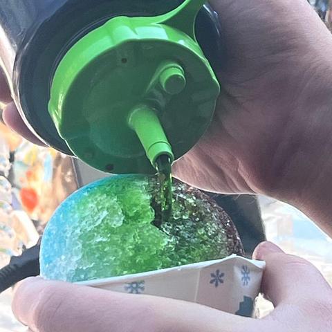 Green syrup being poured over a fresh snow cone